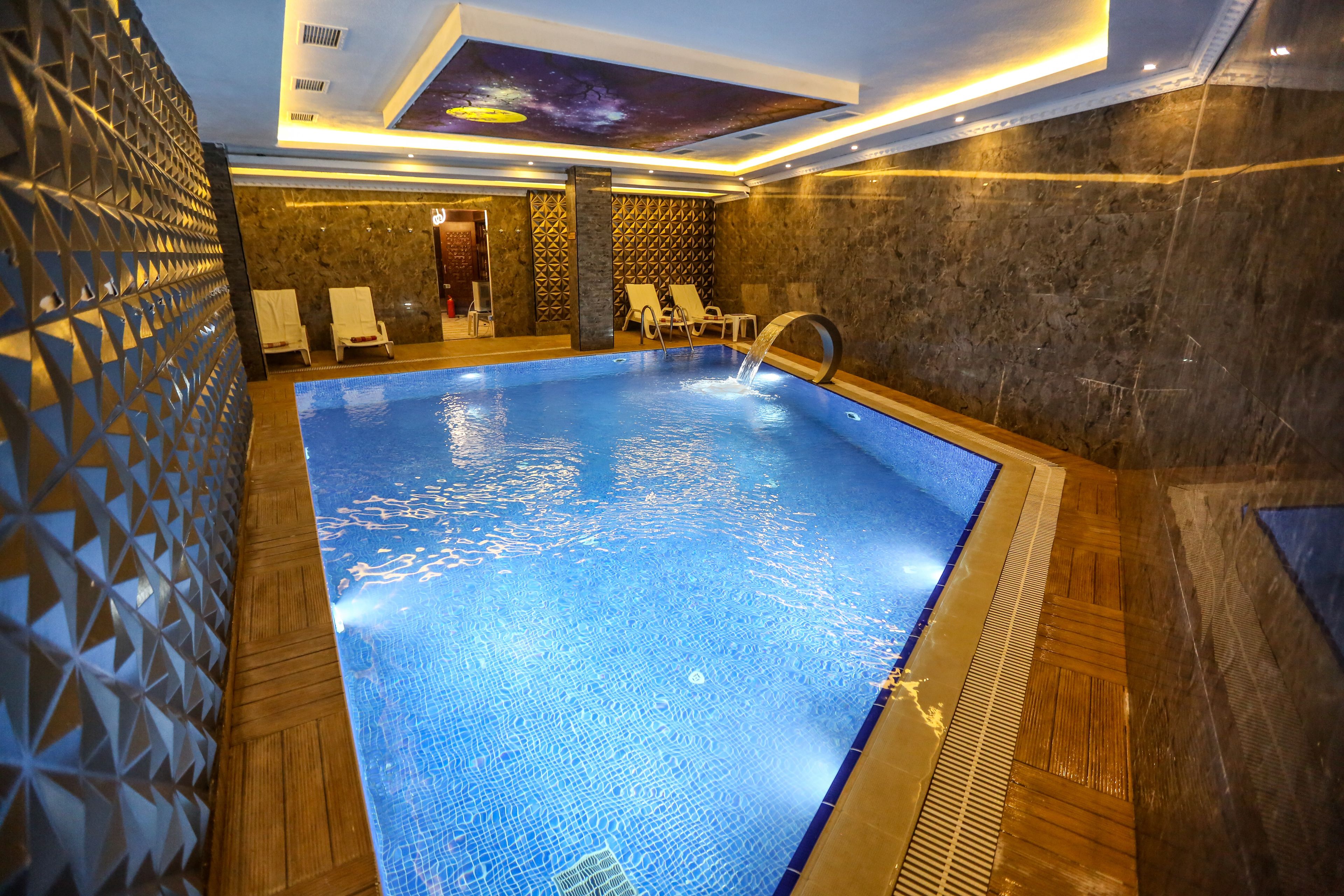 An indoor swimming pool with a geometric wall design, a ceiling mural, and a stone wall.