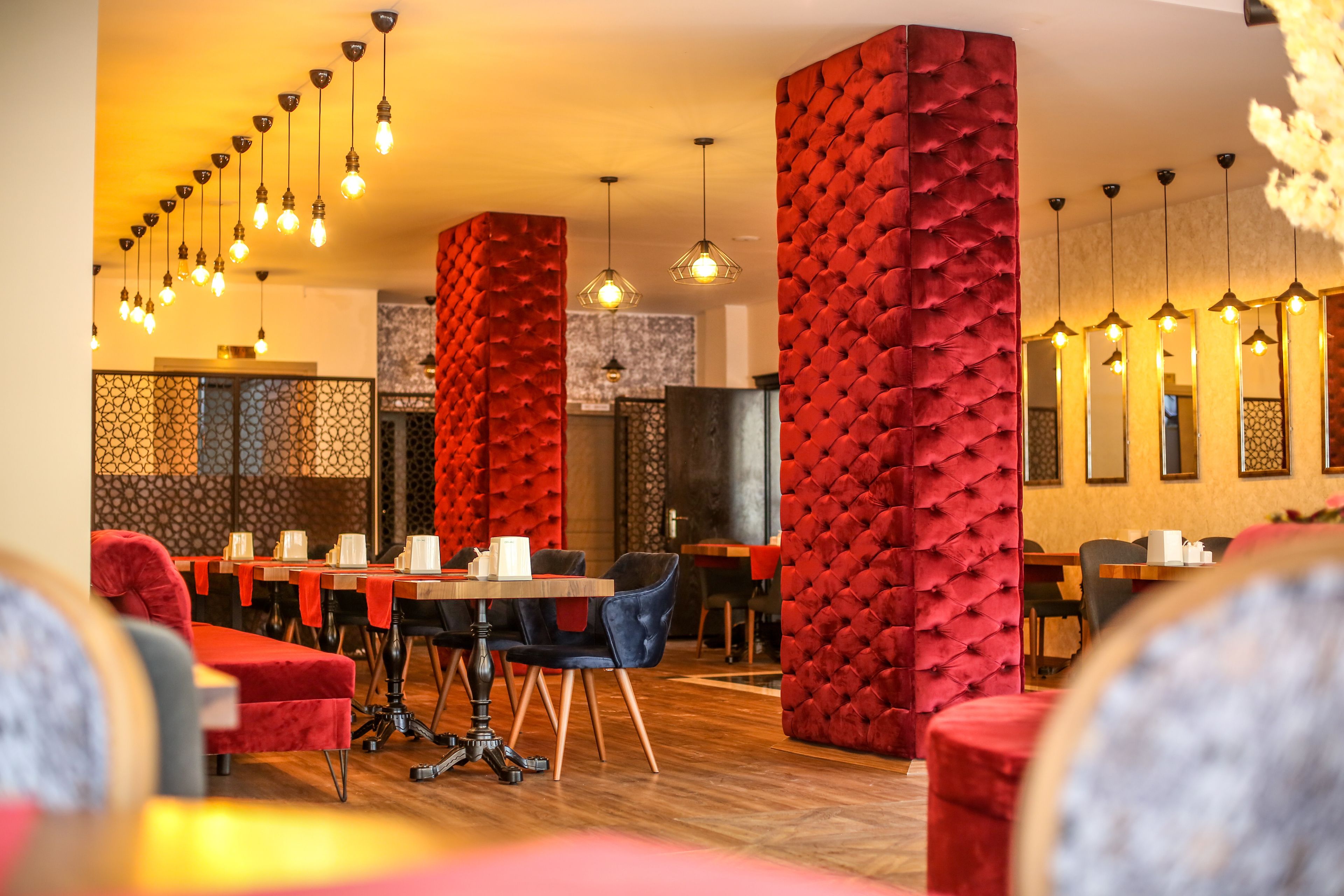 A restaurant interior with red upholstered walls, wooden tables, and hanging pendant lights.
