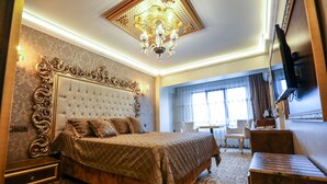 Quarto com cabeceira estofada, lustre, televisão e tapete estampado.