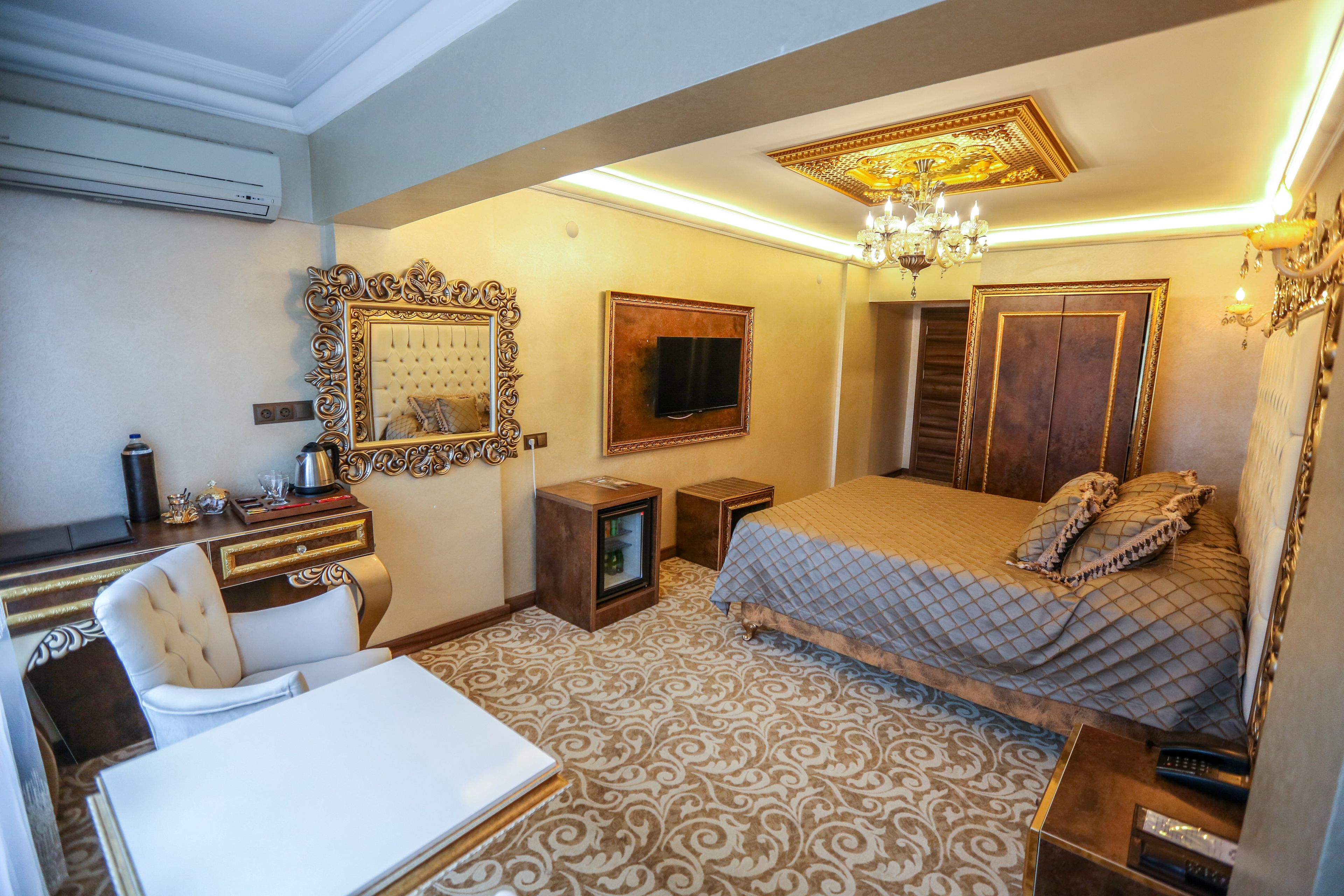 A hotel room with a large bed, a desk with a chair, a television, and a chandelier.