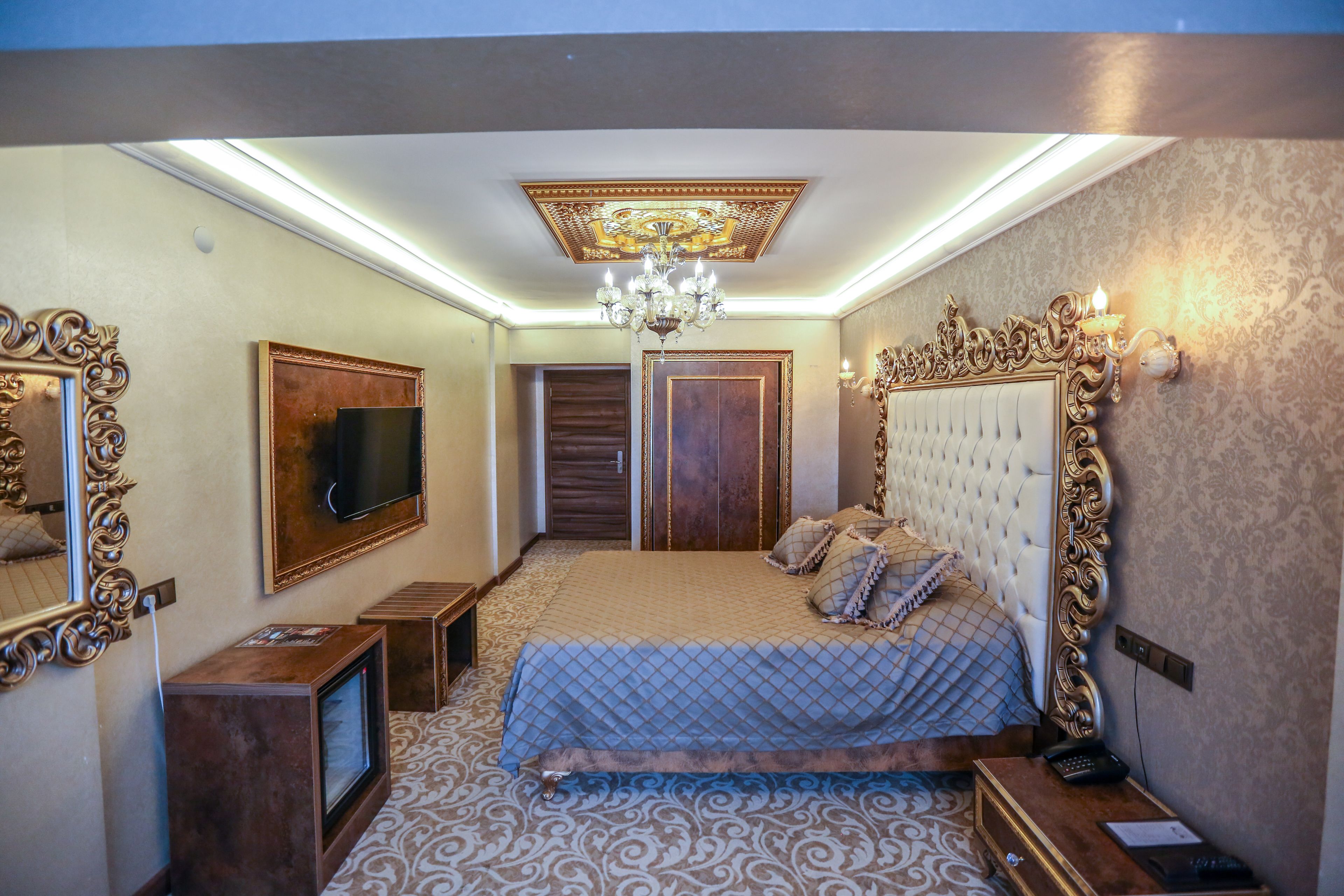 A bedroom with a large bed, a television, a chandelier, and a mirror.