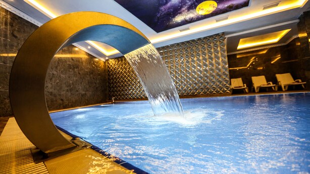 Piscina interior moderna com um elemento aquático, padrões geométricos nas paredes e espreguiçadeiras.