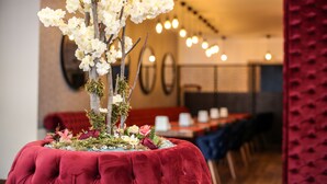 Uma área de refeições com um arranjo floral no centro de uma mesa estofada em vermelho.
