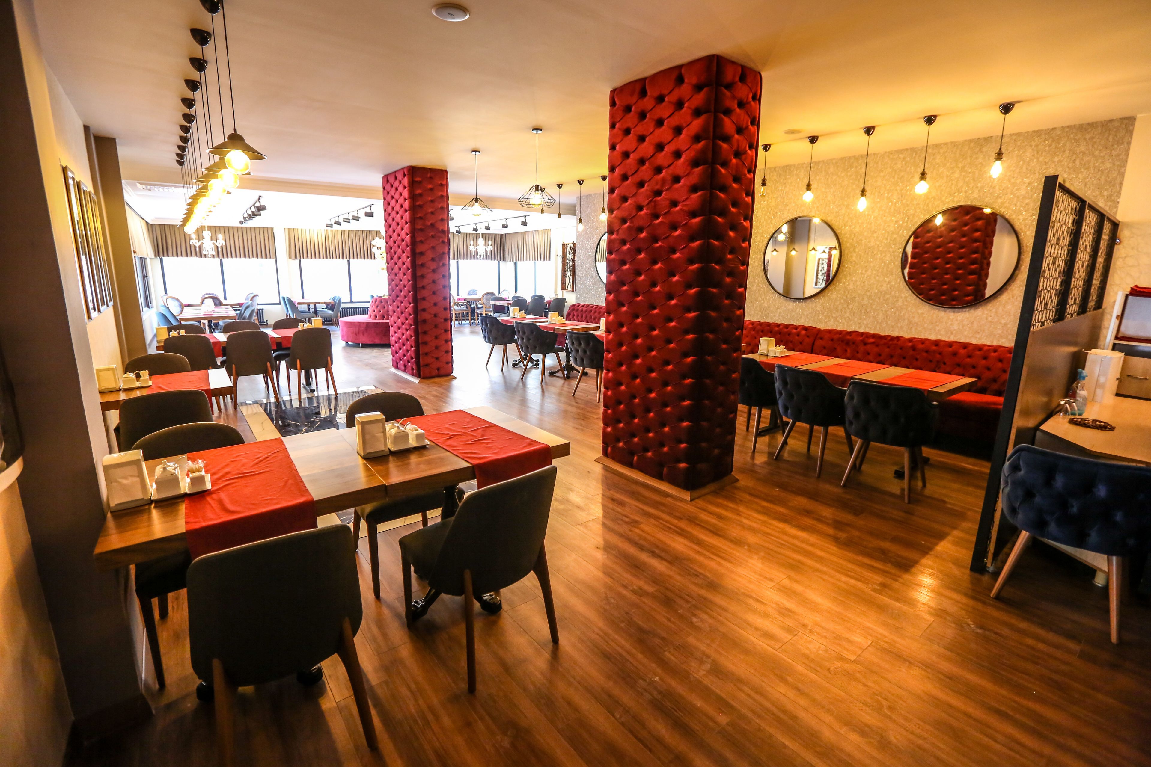 Un restaurante con piso de madera, asientos tapizados en rojo y varias mesas de comedor.