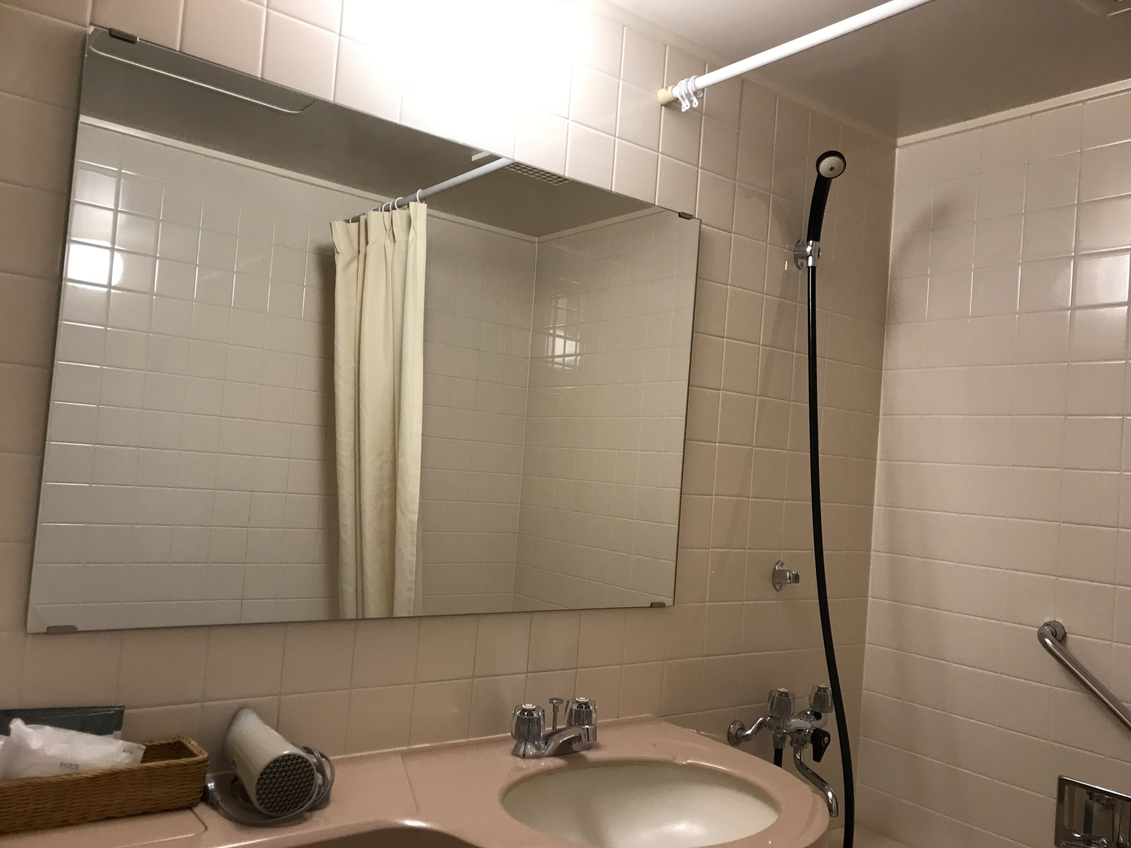 Een badkamer met een wastafel, spiegel, douche en handdoekhouder.