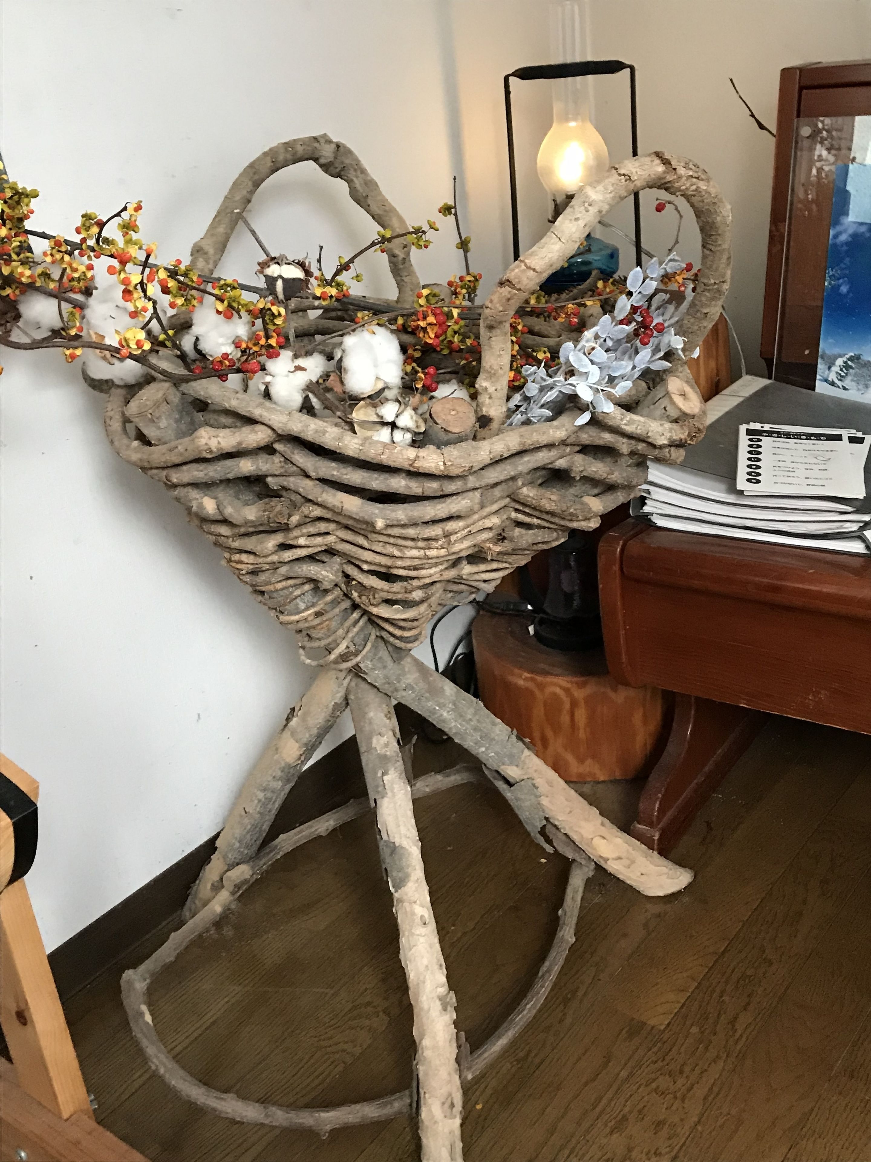 A rustic wooden basket with branches and cotton bolls, placed on a tripod stand.