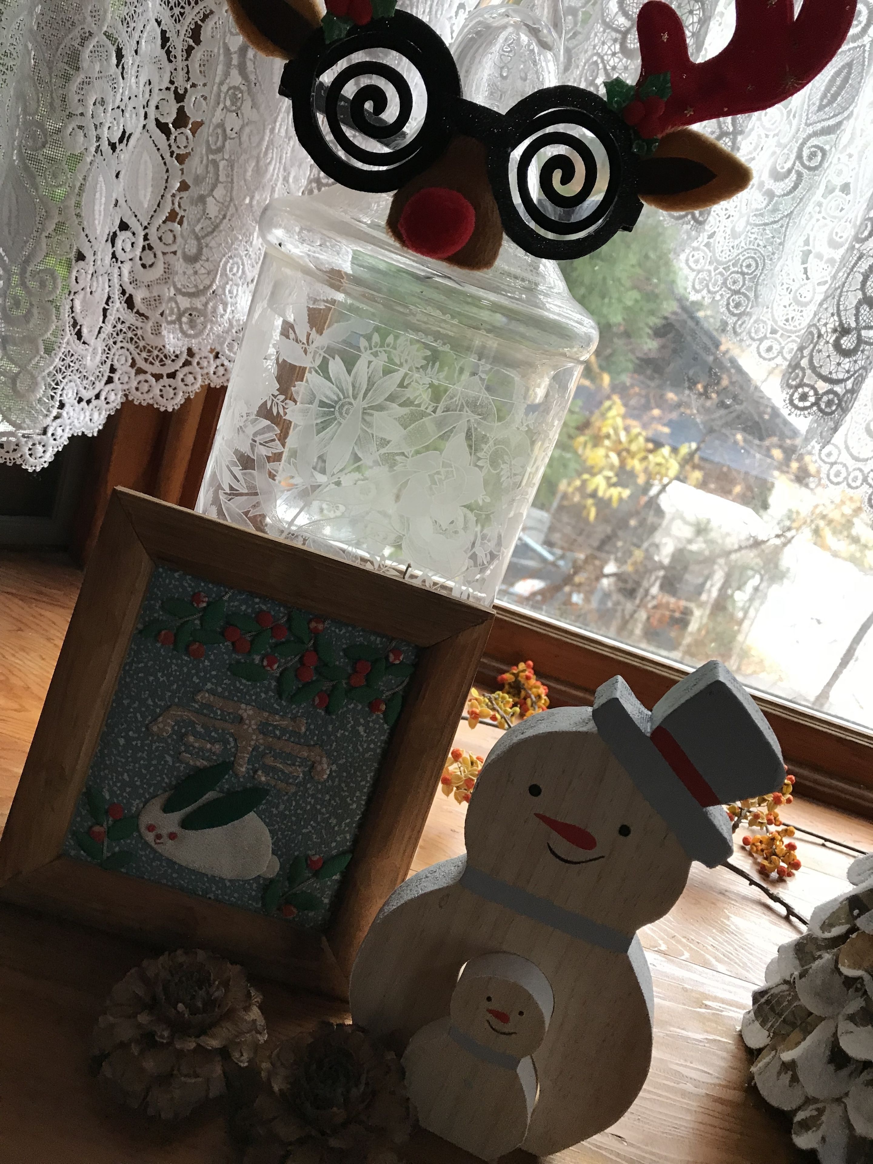 A wooden snowman figure with a hat, a framed picture with a snowman, and a decorative item with reindeer antlers and a red pom-pom.