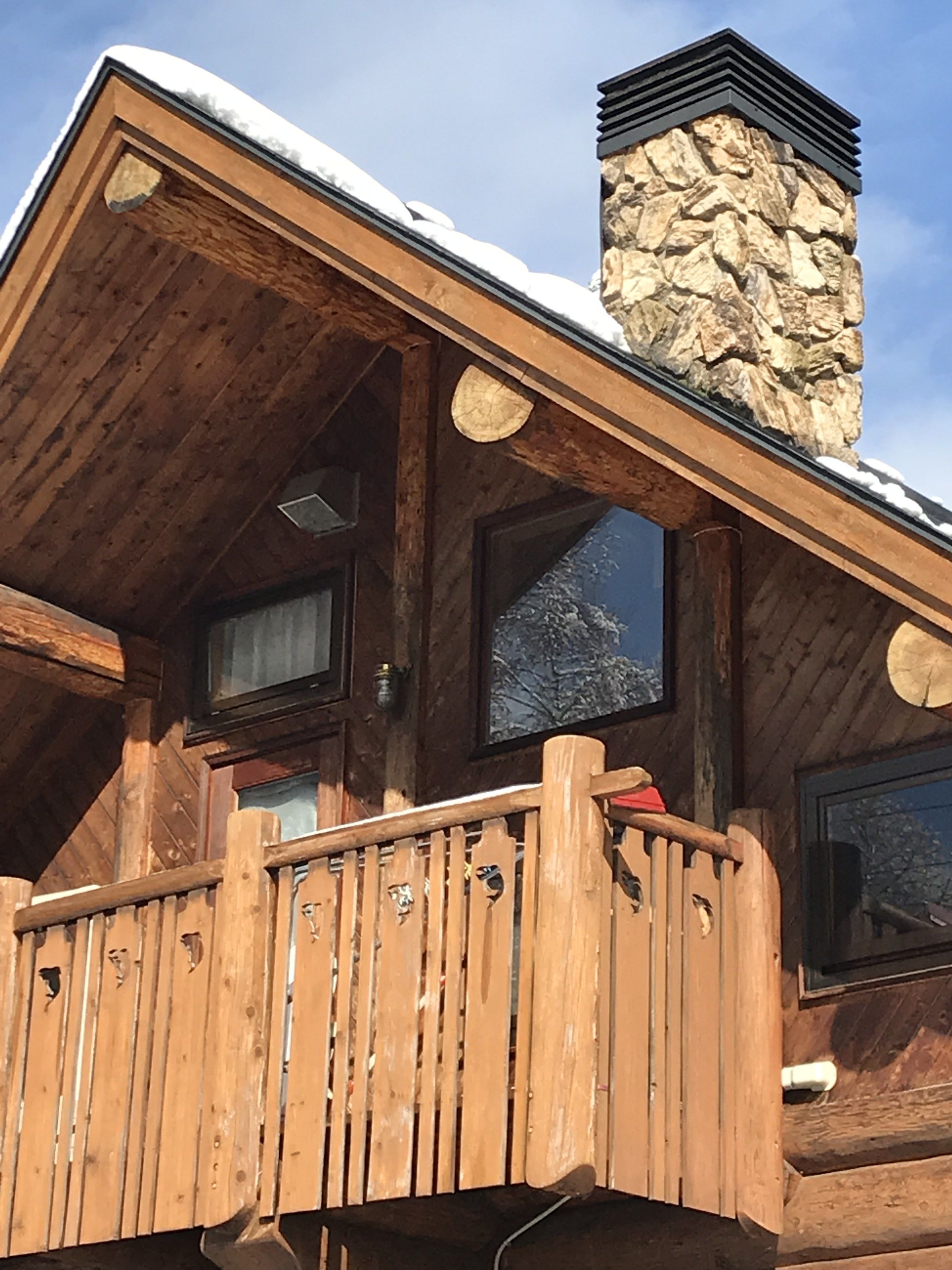 Una cabaña de madera con chimenea de piedra, balcón de madera y ventanas.