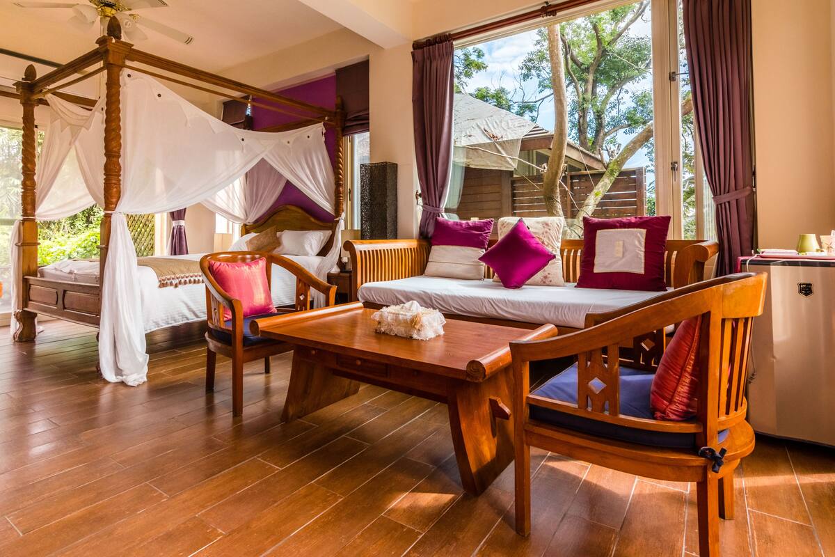 A room with a wooden four-poster bed, a wooden table, and a sofa with cushions.