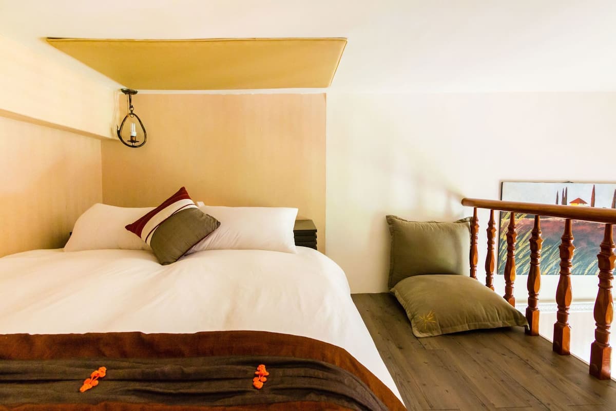 A hotel room with a bed, a nightstand, a wooden railing, and a view of the outside.