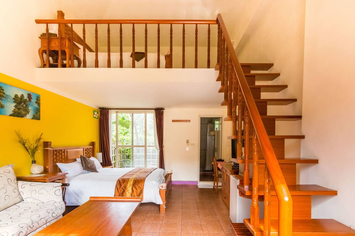 A bedroom with a bed, a sofa, a desk, and a staircase.