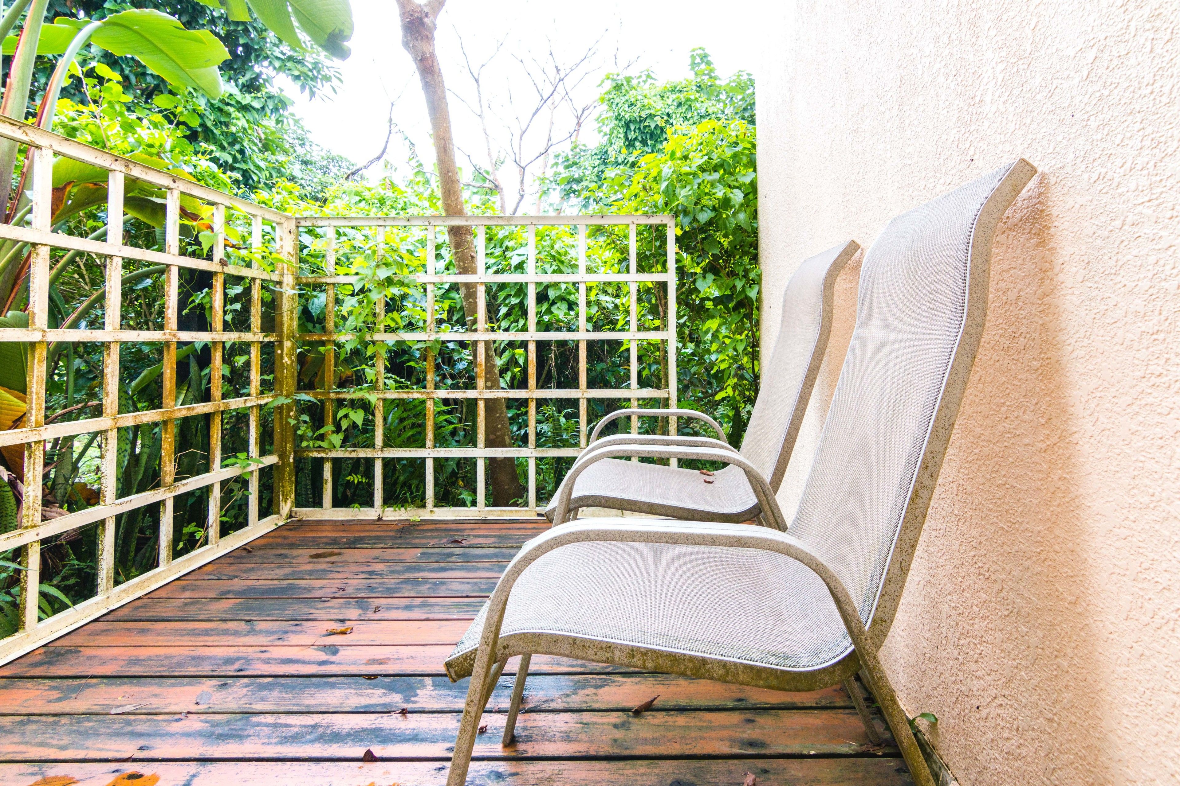 Una terraza de madera con dos sillas de metal y una valla metálica.