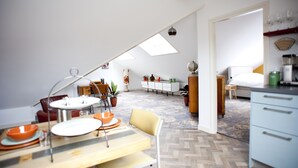 Cozinha moderna com armários brancos, área de jantar com mesa de madeira e quarto mezanino com claraboia.