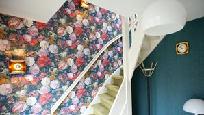 Uma escadaria com papel de parede floral, um relógio de parede branco, um abajur e uma mesa de cabeceira verde.