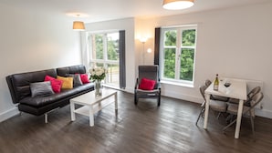 A modern living room with a black leather sofa, a white coffee table, a grey armchair, and a dining table with chairs. - Abodebed - Oval View (Hemel Hempstead)