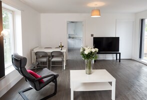 Una sala de estar moderna con comedor, una cocina al fondo y un televisor sobre un mueble.