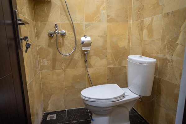 A bathroom with a toilet, a shower, and a marble-tiled wall. - Zenrra House (Bandung)