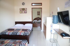 A hotel room with a bed, a desk with a computer, a TV, and a water dispenser. - Zenrra House (Bandung)
