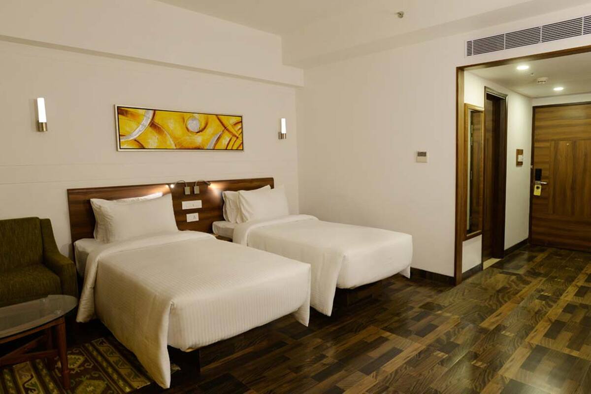 A hotel room with two beds, a sofa, a painting on the wall, and a wooden door.