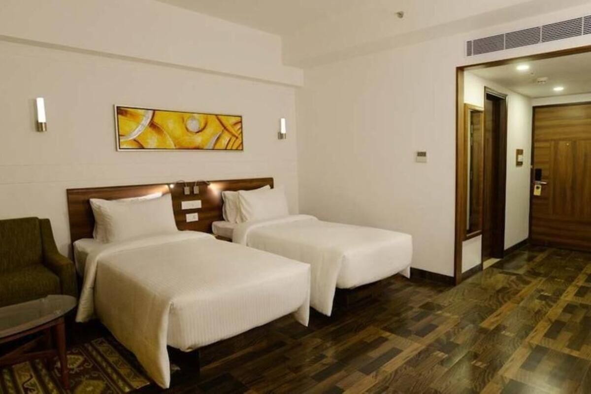 A hotel room with two beds, a sofa, and a painting on the wall.