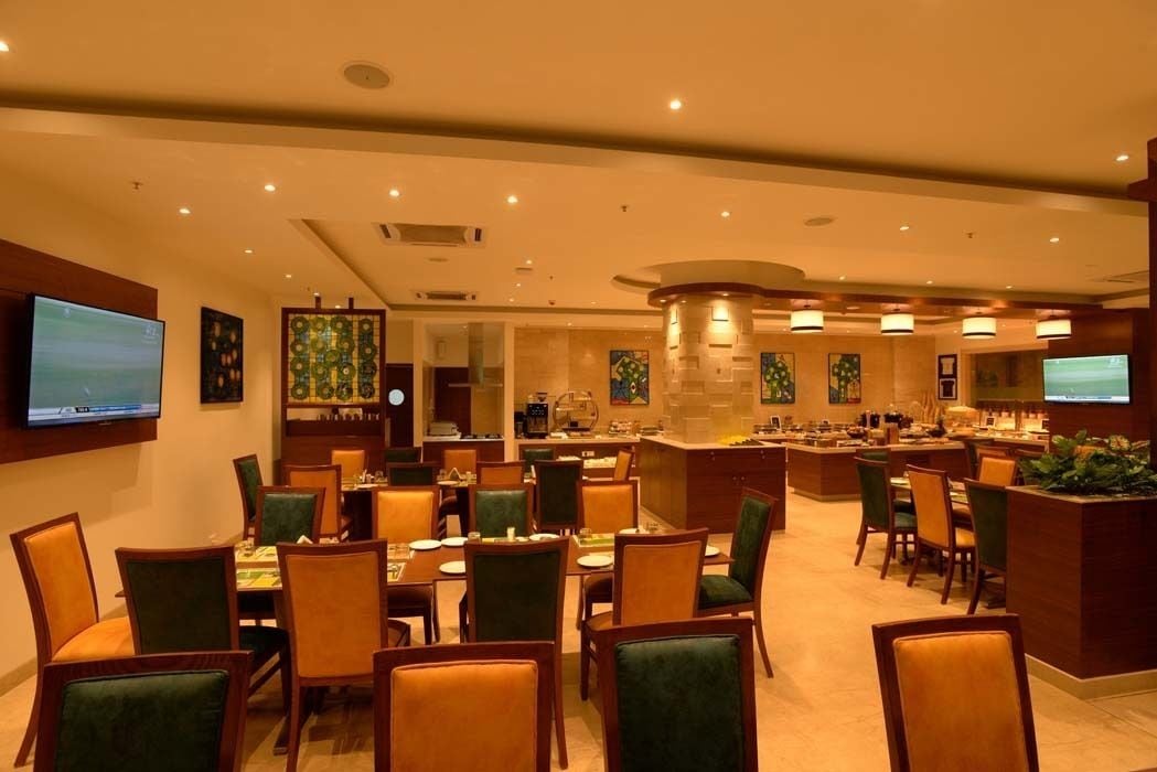 A hotel dining area with multiple tables and chairs, a central bar, and artwork on the walls.