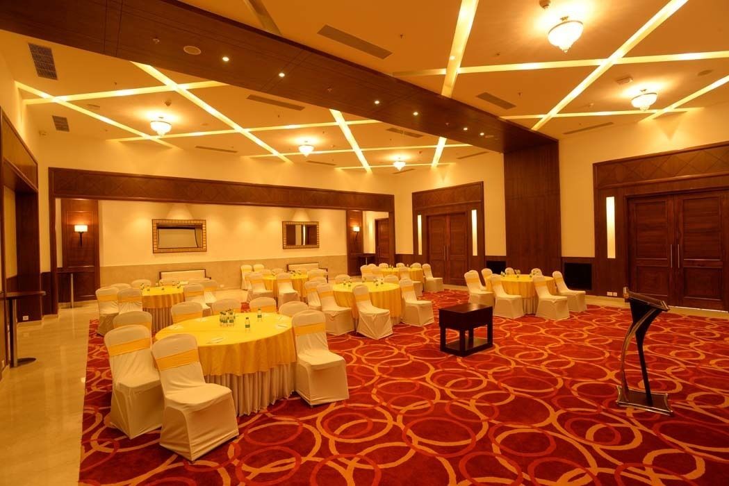 Un salón de conferencias con varias mesas redondas, sillas blancas con cintas amarillas y una alfombra roja con diseño.