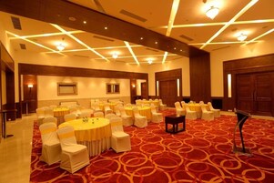 Un salón de conferencias con varias mesas redondas, sillas blancas con cintas amarillas y una alfombra roja con diseño.