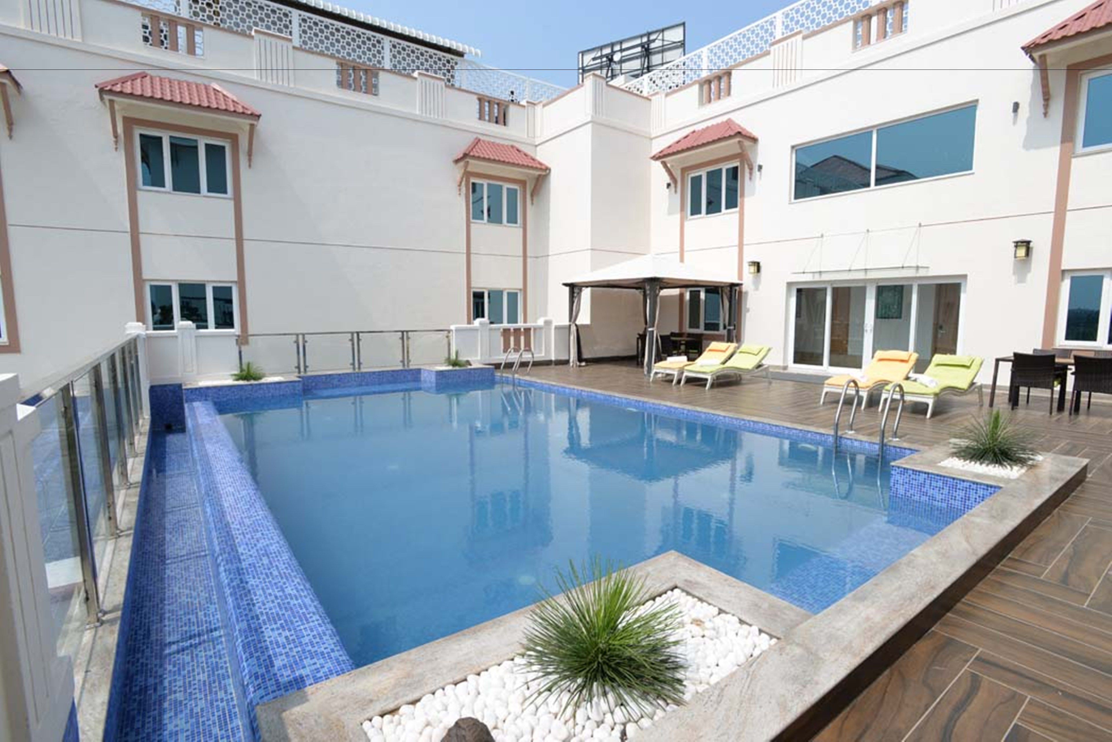 Una piscina con borde de azulejos, rodeada de sillas de descanso y un área de estar cubierta.