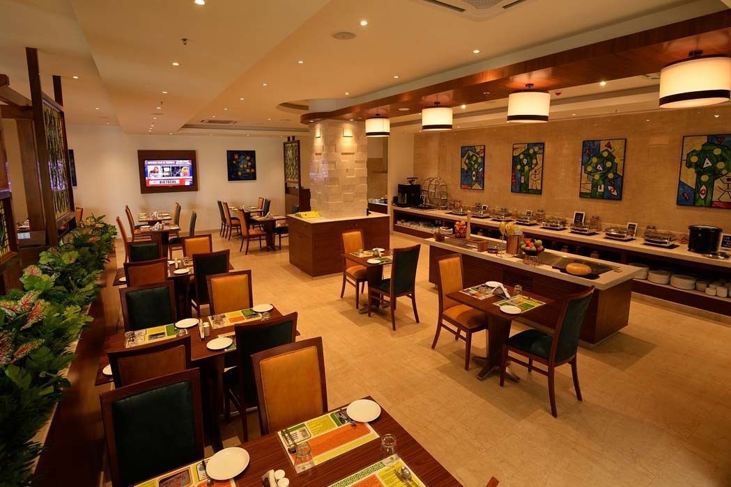 Un comedor de hotel con varias mesas y sillas, una barra de buffet y una pantalla de televisión.