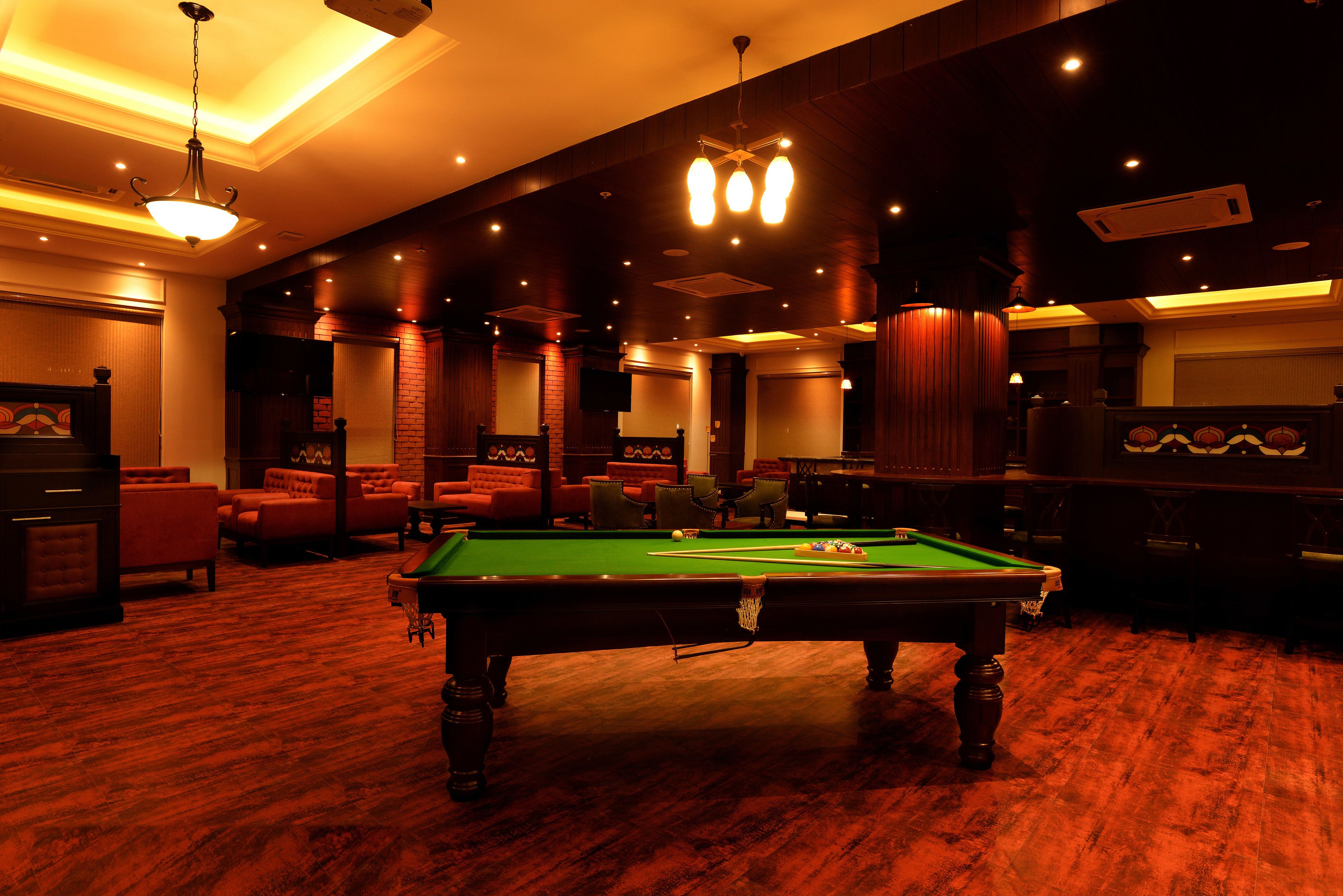 A billiards room with a pool table, red sofas, and a chandelier.