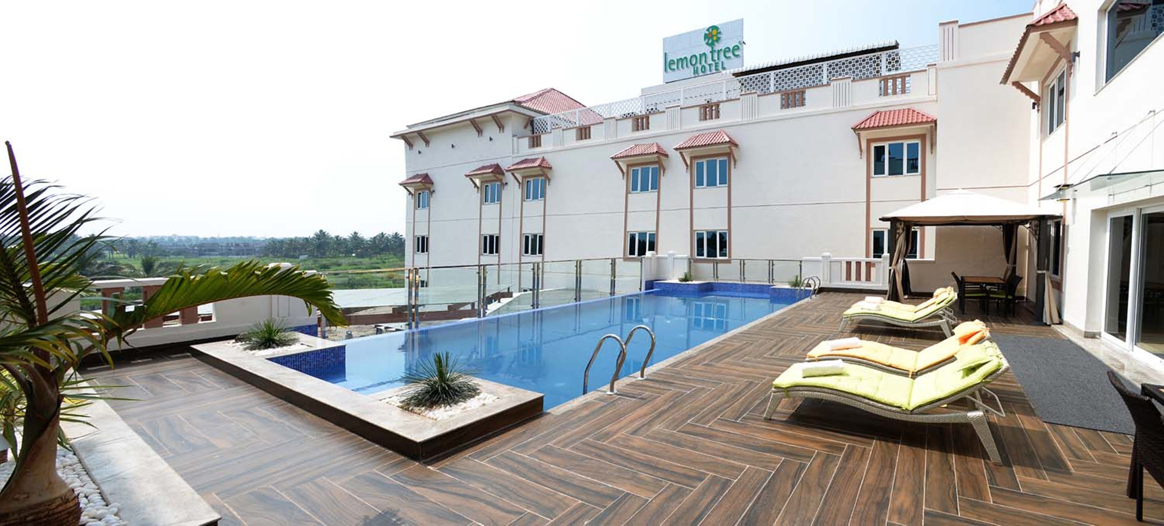A rooftop pool area with lounge chairs and a view of a hotel building.