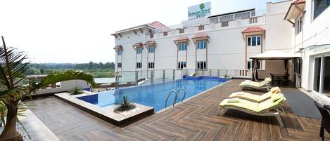 A rooftop pool area with lounge chairs and a view of a hotel building.