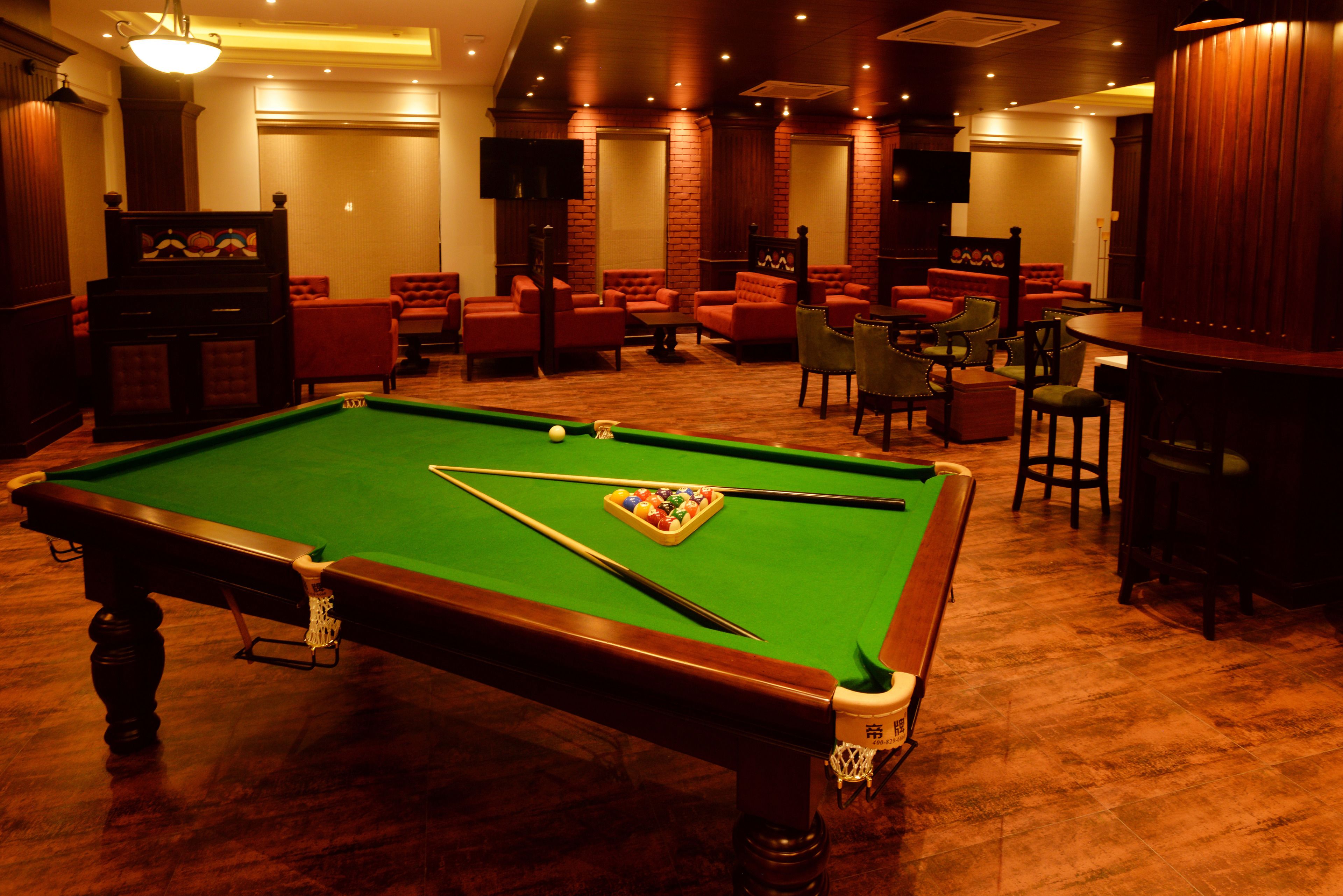 A pool table with a green felt surface, surrounded by red upholstered chairs and a bar area with stools.