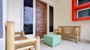 Una habitación con un banco de madera, un taburete verde y una puerta que da a vista de un edificio.