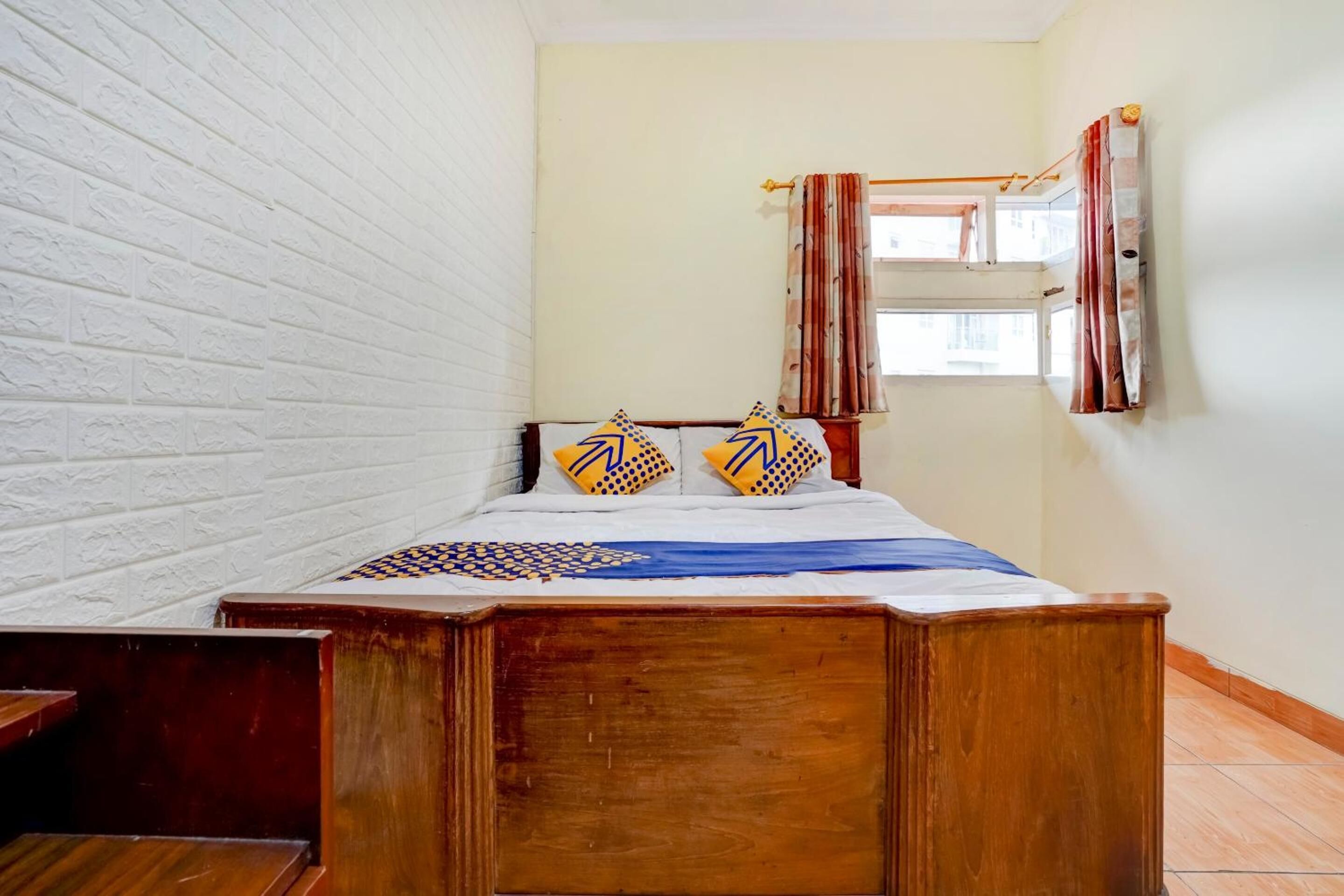 A bedroom with a wooden bed, white brick walls, a window with curtains, and a small bedside table.