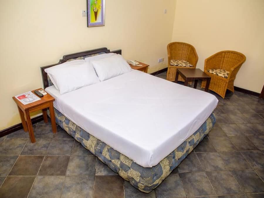 A neatly made bed with white linens, a small wooden nightstand with a phone and a magazine, and two wicker chairs with cushions.