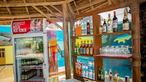 Un espace bar équipé d’un distributeur de bière réfrigéré, d’étagères remplies de boissons en bouteille et d’une variété de verres.