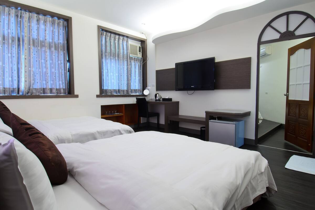 A hotel room with two beds, a desk with a computer, a TV mounted on the wall, and a large mirror.