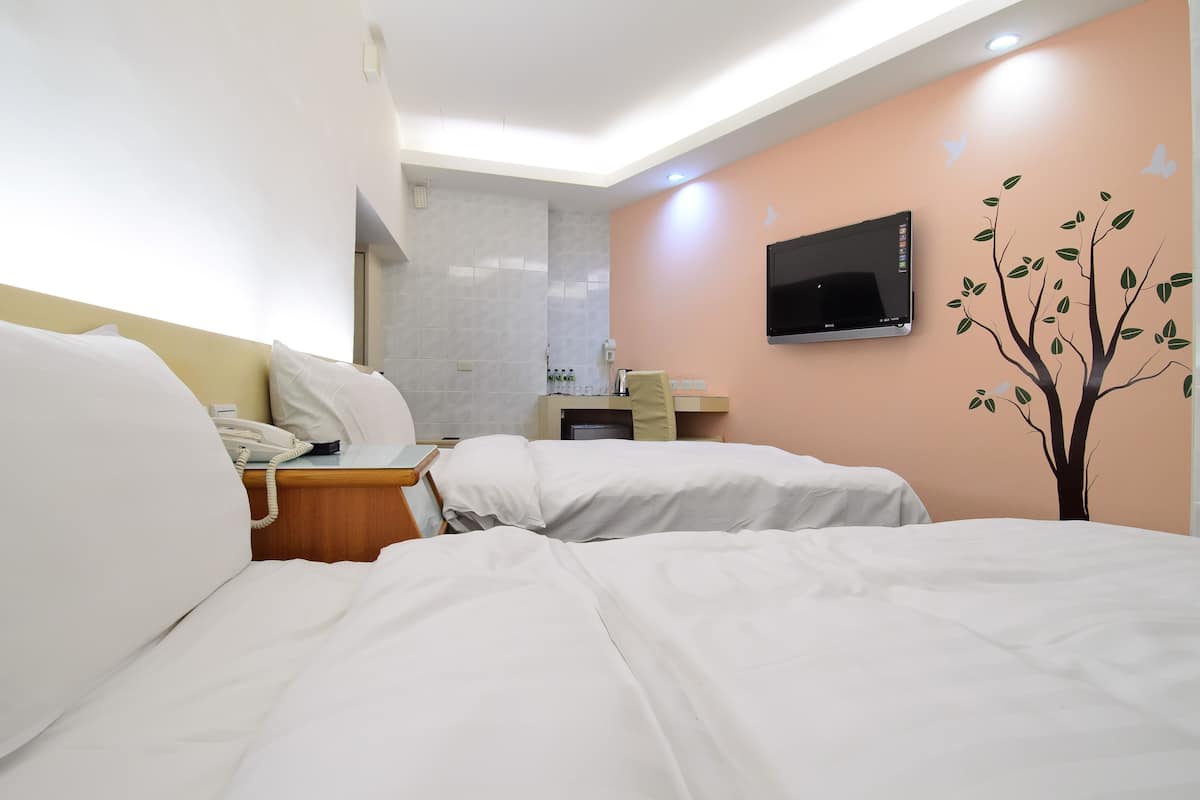A hotel room with two beds, a TV mounted on the wall, and a small desk with a telephone.