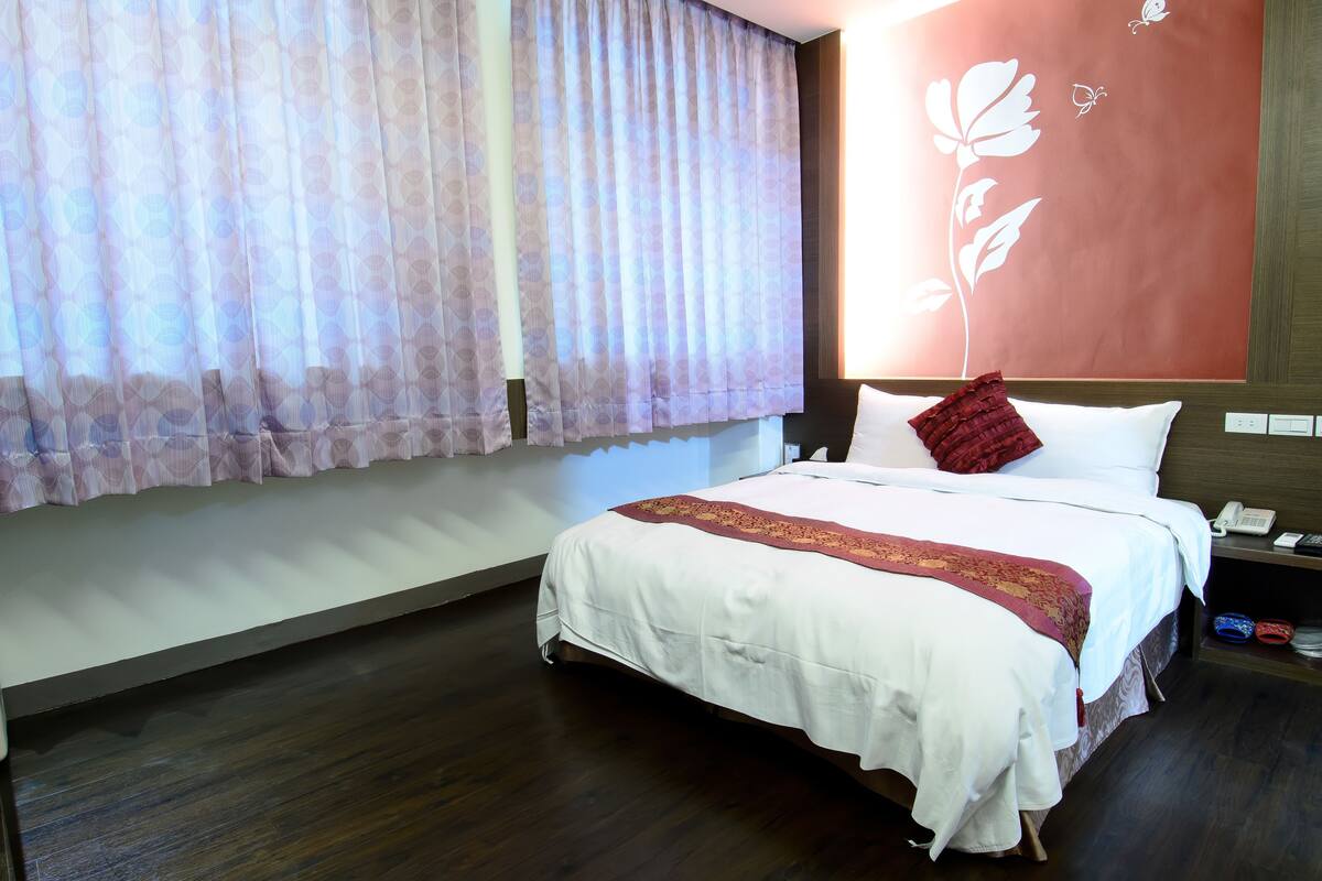 A hotel room with a large bed, a bedside table with a phone, and a wall with a floral design.