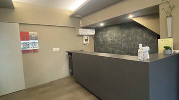 A hotel reception area with a modern design, featuring a reception desk, a wall-mounted air conditioning unit, and a small potted plant.