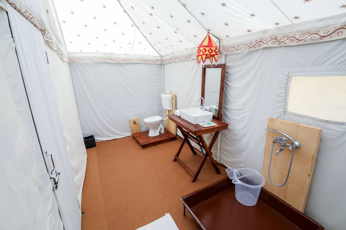 Habitación con carpa, una mesa de madera, lavamanos, inodoro y zona de ducha.