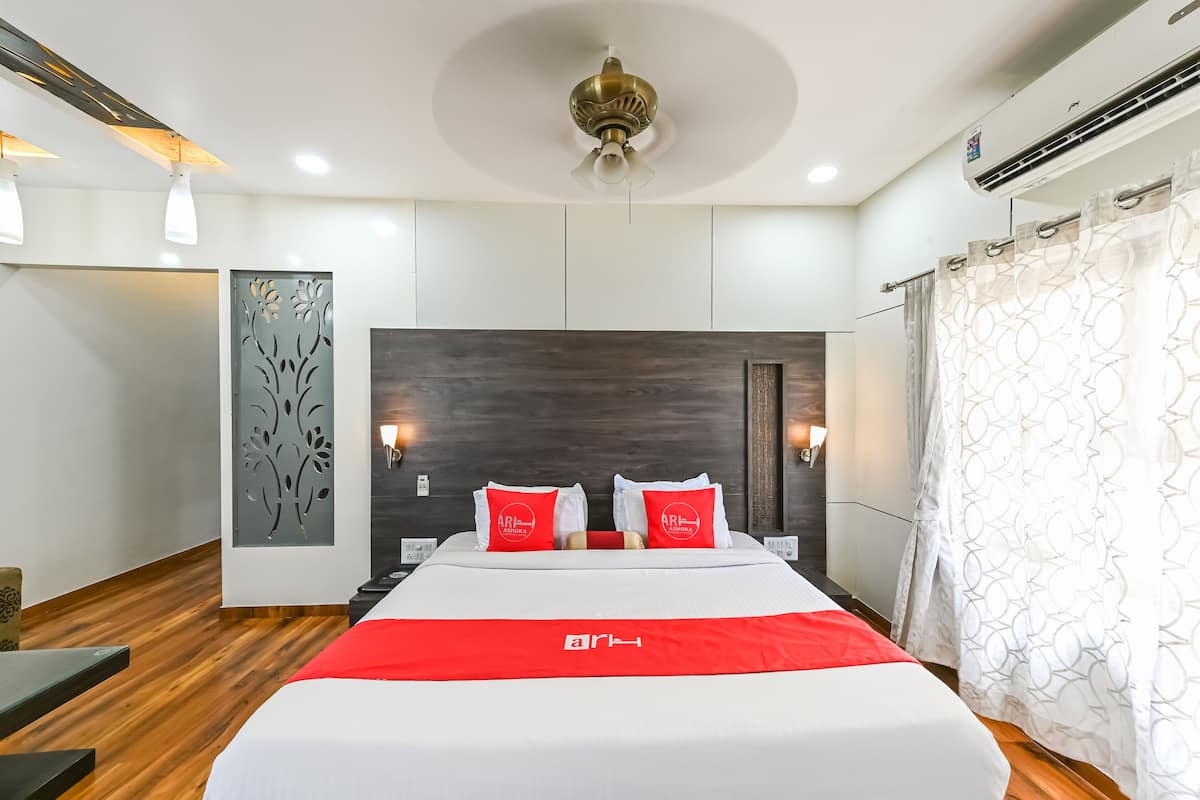 A modern hotel room with a large bed, a dark wood headboard, and a red accent on the bedspread.