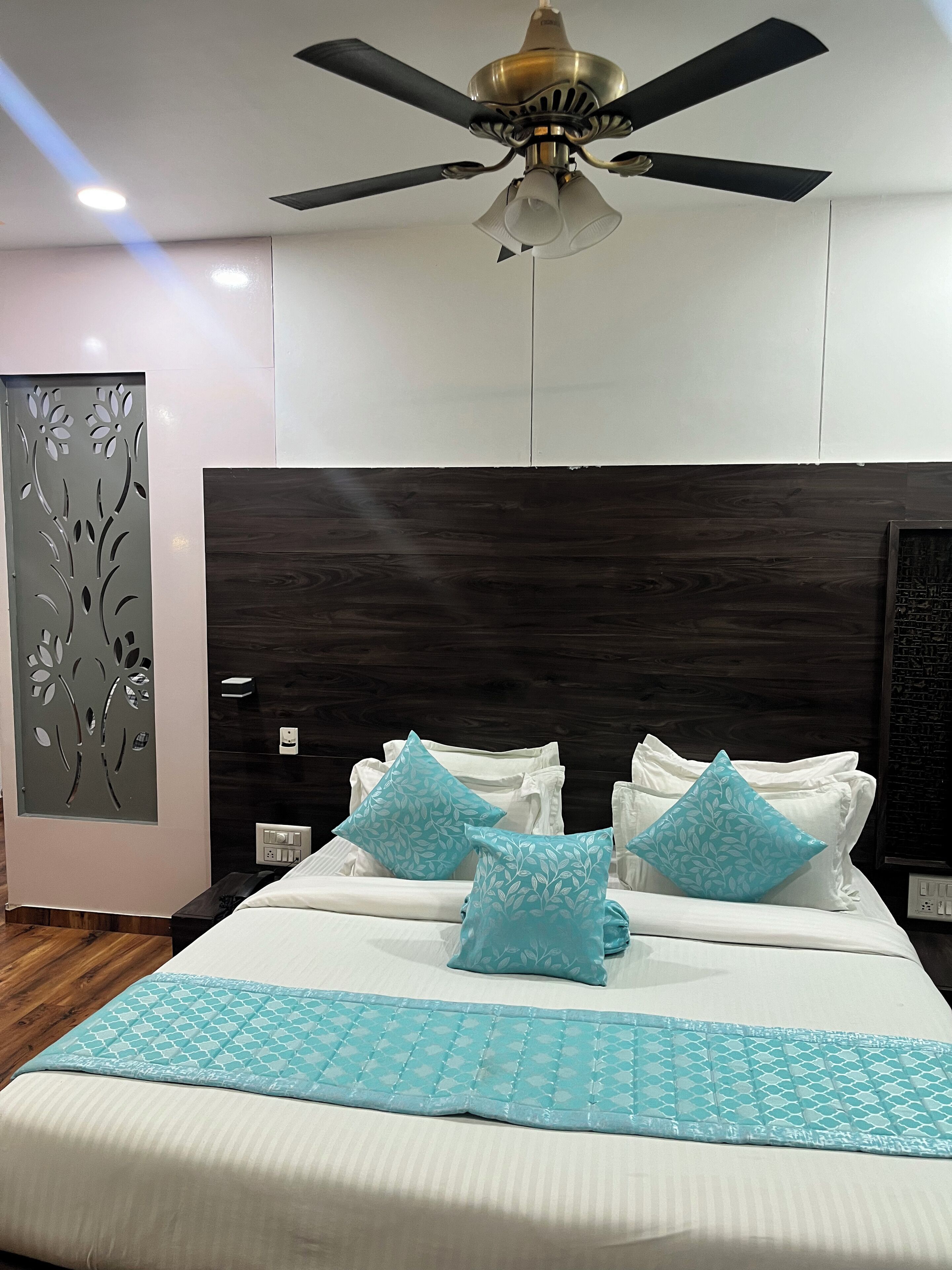 Una cama bien hecha con ropa blanca y almohadas estampadas en azul, un ventilador de techo y un cabecero de madera oscura.
