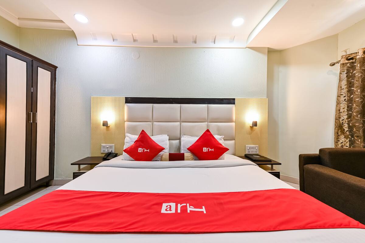 A hotel room with a large bed, two bedside tables, a nightstand, a chair, and a wardrobe.