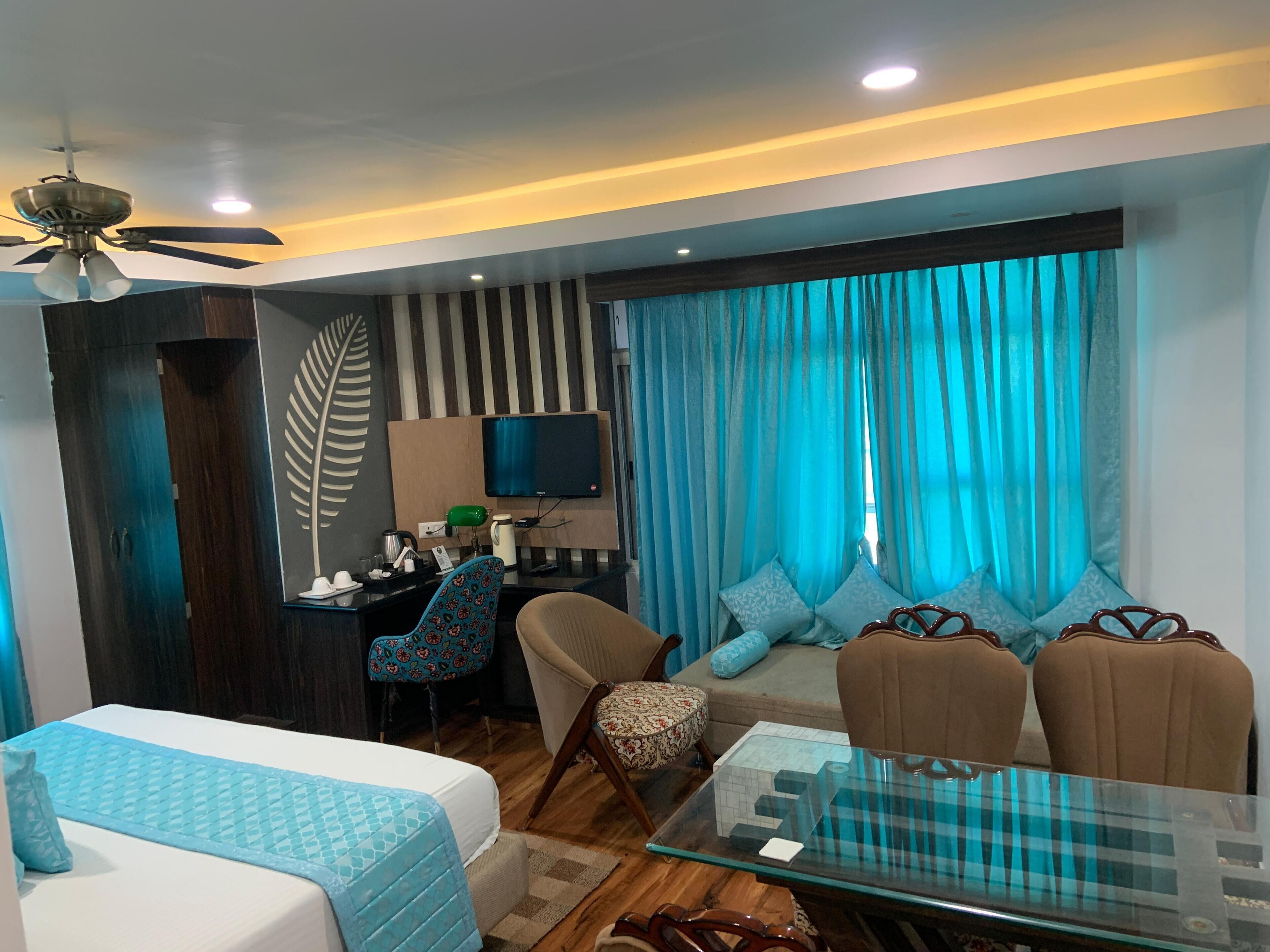 Una habitación de hotel moderna con cama, escritorio con computadora, sofá y mesa de centro de vidrio.