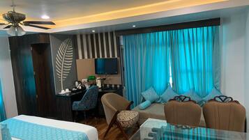 Una habitación de hotel moderna con cama, escritorio con computadora, sofá y mesa de centro de vidrio.