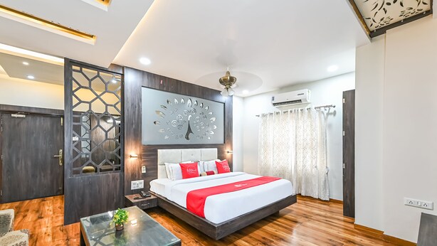 A modern bedroom with a large bed, wooden flooring, a glass coffee table, and a decorative wall piece. - Ashoka Residency Hotel (Bhilwara)