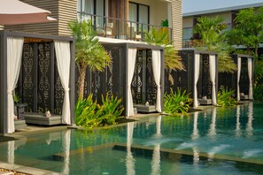 Zona de piscina con múltiples sillas de descanso y un área de estar cubierta con cortinas.