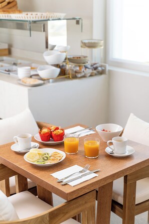A breakfast table with plates of food, cups, and a glass of orange juice. - Kallos of Mykonos (Mykonos)